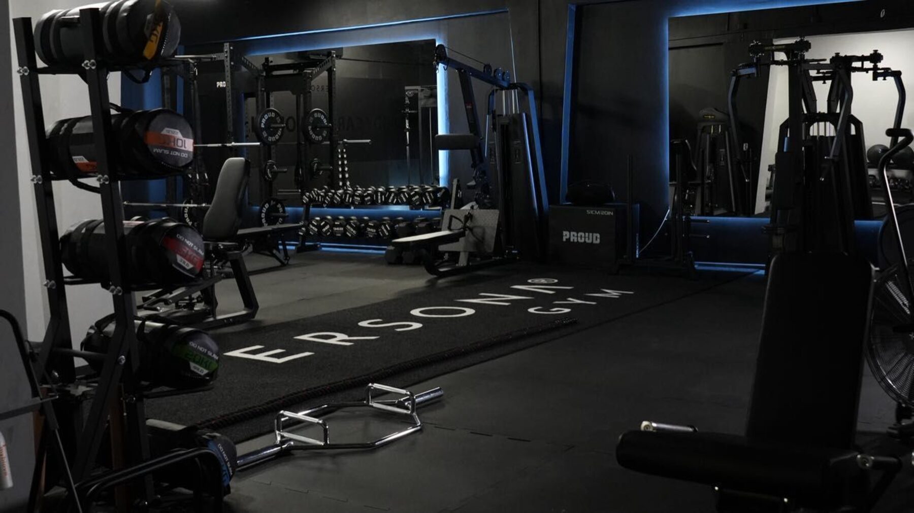 Sala treningowa Persona Gym z niebieskim podświetleniem, matą z logo i stojakami na ciężary